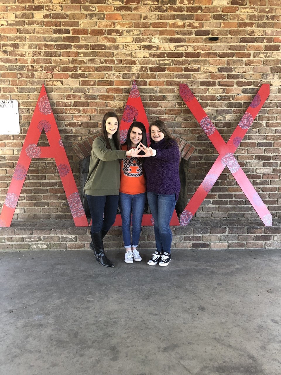 Members of Alpha Delta Chi in front of large letters throwing the organization sign with their hands. 